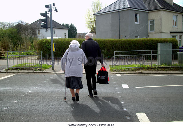 old-couple-crossing-road-at-traffic-lights-with-walking-stick-hyk3fr